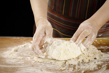 Hands kneading fresh wheat dough with flour on wooden cutting board - homemade bread baking process