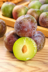 Fresh Sichuan Plums Closeup with Cut Half Showing Green Flesh and Pit on Wooden Surface