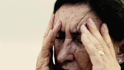 Elderly woman massaging her temples with eyes tightly shut, intense focus on relieving pain or...