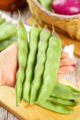 Fresh Green Pea Pods in Hand on Wooden Base with Vegetable Basket