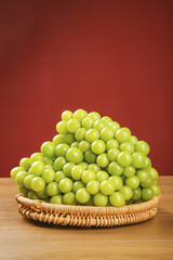 Fresh Green Seedless Grapes in Wicker Basket on Wood Table Red Background