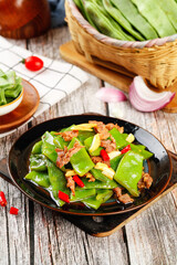 Stir-Fried Green Snow Peas with Red Peppers and Meat in Black Pan on Rustic Wooden Kitchen Table