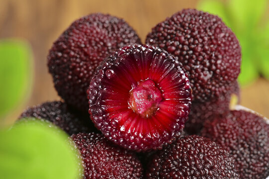 Fresh Chinese Bayberry Yangmei Fruit Cut Open Showing Red Flesh and Textured Skin on Wood Surface