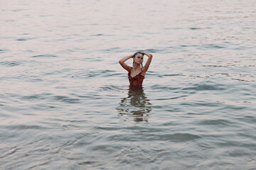 Woman standing in calm water wearing a red dress at sunset, serene mood, peaceful atmosphere, natural background