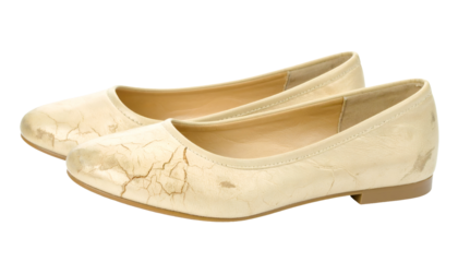 Worn cracked beige leather women’s flats pair with scuffs and aged patina on isolated background