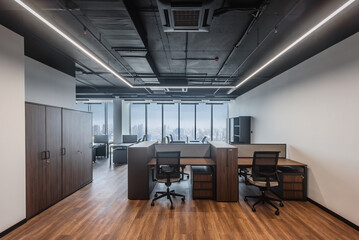 Corporate coworking loft with desks in row and panoramic window. Contemporary shared workspace with ergonomic chairs and large windows