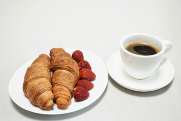 Croissants and fresh strawberries on plates next to a cup of coffee