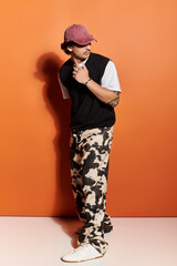 Stylish young man showcasing fashion sense against a vibrant orange backdrop in urban setting