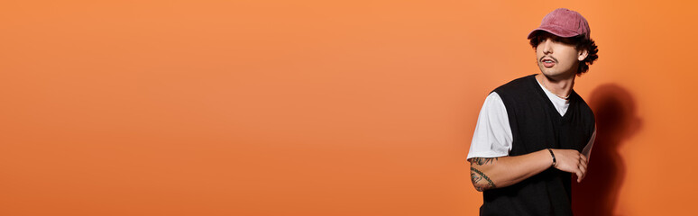 A handsome young man showcases his unique style with a trendy outfit in a bright orange setting