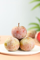 Fresh Garden Plums on White Plate with Green Foliage Background