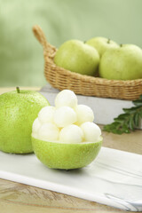 Fresh Green Pears in Wicker Basket with Carved Pear Bowl on Wooden Table