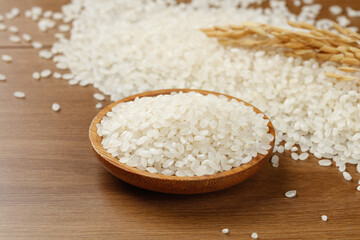 Fresh White Rice Grains in Wooden Bowl with Wheat Stalks on Rustic Wood Table Background