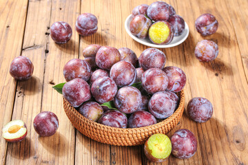Fresh Red and Purple Plums in Wicker Basket on Rustic Wood Table with Cut Fruit Showing Golden Flesh