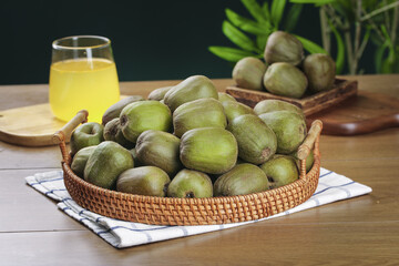 Fresh Kiwi Fruits in Wicker Basket on Wood Table with Juice Glass and Green Plants Background
