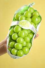 Fresh Green Grapes in Package Held by Hand on Yellow Background