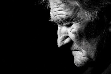 Pensive elder man with grey hair looking down on black background
