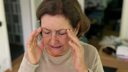Mature woman experiencing intense headache or stress, holding head with both hands, expressing...