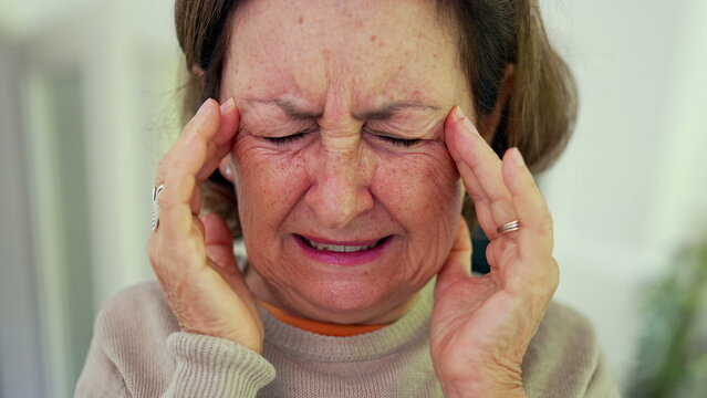 Mature woman experiencing severe headache, squeezing eyes shut, and holding head with both hands, displaying visible discomfort. Wrinkles and facial expression, emotional pain-SD 480p