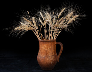 Clay jug filled with dried wheat stalks against a dark background showcasing rustic decoration
