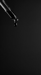 A clear glass dropper with a dark liquid inside holds a single suspended drop against a stark black background, emphasizing precision and scientific application.