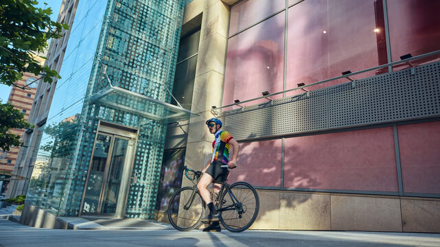 Cyclist resting with road bike near glass building in urban environment. Concept of active lifestyle, modern city transport, sports culture, fitness, and emotional pause. - Powered by Adobe