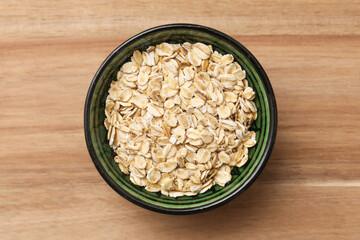 Bowl with oatmeal flakes on wooden table. Healthy breakfast ingredient closeup. Organic diet food. Natural nutrition for vegetarian lifestyle. Rustic agriculture product detail.