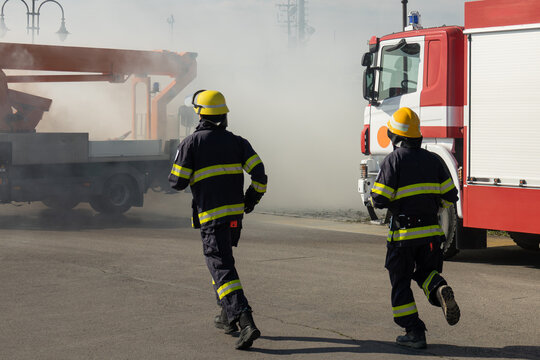 Two brave firefighters in full uniform running into action. Emergency response team rushing towards a fire scene with thick smoke and a fire truck during a rescue mission.