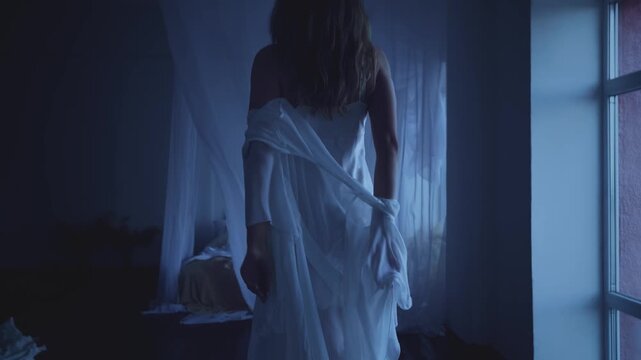 Beauty adult woman throws off dressing gown silk peignoir robe goes to sleep on canopy bed in short hot dress, white curtains fly wind, window dark room night blue light. girl sexy body back rear view
