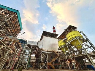 Industrial plant with striking metal structures and yellow silos against a bright sky offering a detailed view of modern manufacturing and infrastructure design with a red and white chimney © agung