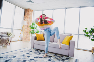 Young woman enjoying music with headphones, dancing happily in a cozy apartment living room with colorful cardigan