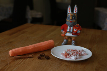 A decorative rabbit figurine with carrots, spices, and a sweet treat on a wooden table.