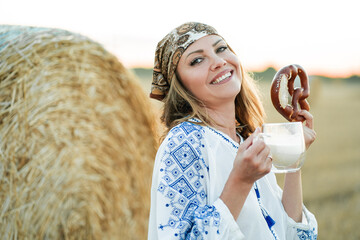 Woman 40s years old in a field with hay bales is enjoying the evening, drinking milk and eating...