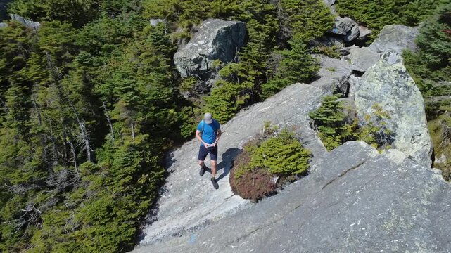Male model hiker backpacker hiking across rocky mountain top terrain through green forest summit. Aerial shot with a drone for incredible landscape and surroundings.