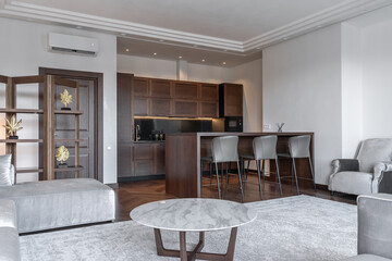 large modern living room combined with kitchen. Grey sofa, parquet flooring, wooden kitchen furniture, kitchen table and chairs.