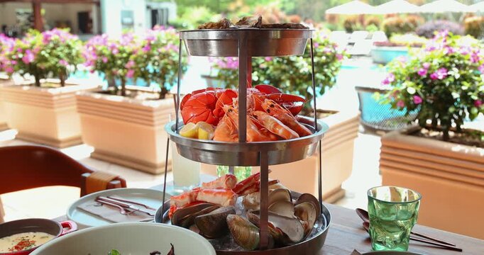 Luxurious seafood platter served poolside at resort. Fresh lobster, shrimp, clams create elegant dining experience. Outdoor setting with vibrant flowers adds sophistication.