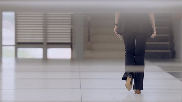 Lower body rear shot of businesswoman in black slacks walking confidently with tablet, representing new opportunities and goals.