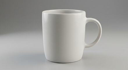 Obraz premium A classic plain white ceramic coffee mug with a handle, ideal for hot drinks, standing isolated against a seamless light grey studio background