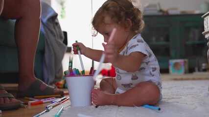 Toddler sitting on floor playing with colorful markers and emptying container, showing curiosity, exploration, and early learning through creative play indoors