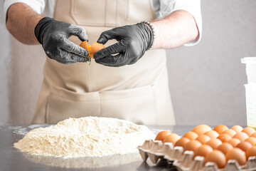 Chef cracking egg over flour mound on kitchen counter, wearing gloves and apron. Baking preparation...