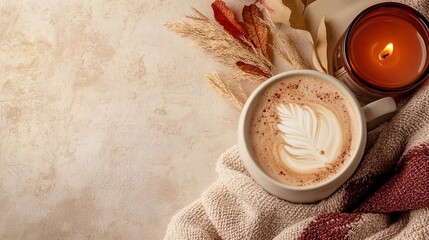 Cup of autumn coffee with latte art, candle, dried leaves and cozy blanket in a warm flat lay scene with copy space, perfect for seasonal banner or fall-inspired mockup