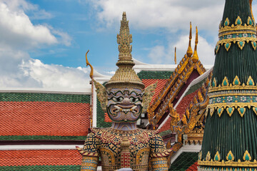 Fototapeta premium Giant statue at Grand Palace, Bangkok - A close-up of a giant mythological statue (Yak) at the Grand Palace, with ornate details and traditional Thai rooftops in the background.