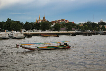 Puente colgante and Bangkok skyline - A longtail boat floats on the Chao Phraya River with the ornate architecture of a Thai temple and the modern city skyline in the background.