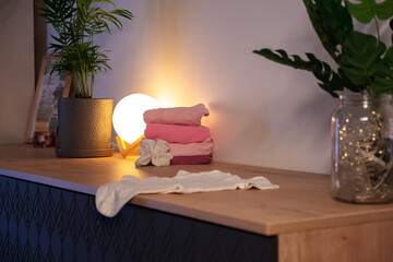 a stack of pink baby clothes in warm muted light. anticipation getting ready for the baby girl at home