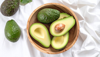 Close-up shot of fresh avocados, some sliced, arranged in a wooden bowl on a white cloth.