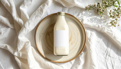 A glass bottle of milk sits on a plate, surrounded by a white cloth and flowers.