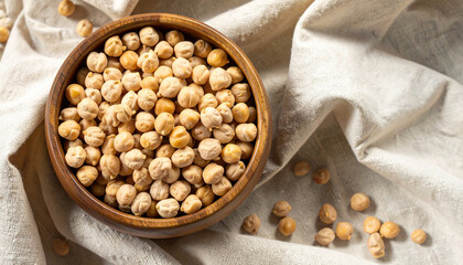 Close-up shot of a wooden bowl filled with dried chickpeas, sitting on a white cloth.