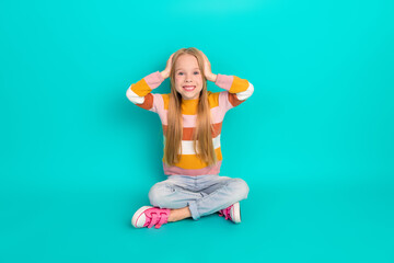 Smiling girl sitting cross-legged on teal background wearing striped sweater showcasing joy and playful expression