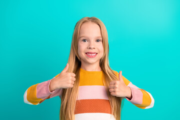 Adorable young girl with long blonde hair showing thumbs up gesture, wearing a colorful striped sweater on a teal background