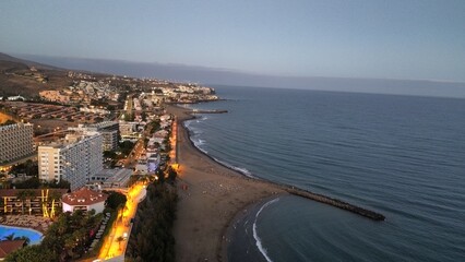 Moon rising over coastal city at dusk with illuminated buildings and sandy beach © laurentiu