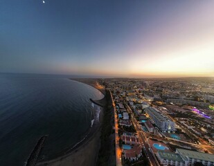 Moon rising over coastal city at dusk with illuminated buildings and sandy beach © laurentiu